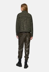 Green leopard print jacket with a pleated back, paired with shiny, dark olive patterned pants and black chunky boots.