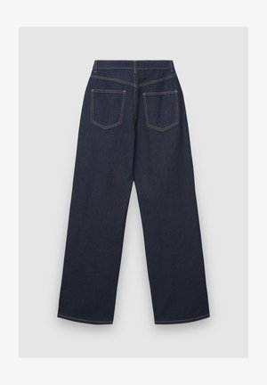 Jean large en denim bleu foncé avec une texture lisse, deux poches arrière et des coutures jaunes le long des coutures.