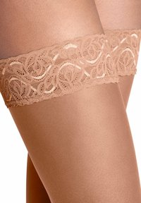 Bas autofixants couleur chair avec un haut en dentelle beige texturée présentant des motifs complexes de volutes et des bords festonnés, couvrant la jambe de manière lisse en dessous.