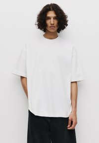 Witte oversized t-shirt van katoen, met een ronde hals en korte mouwen, gecombineerd met donkere denim shorts. Eenvoudig en minimalistisch ontwerp.