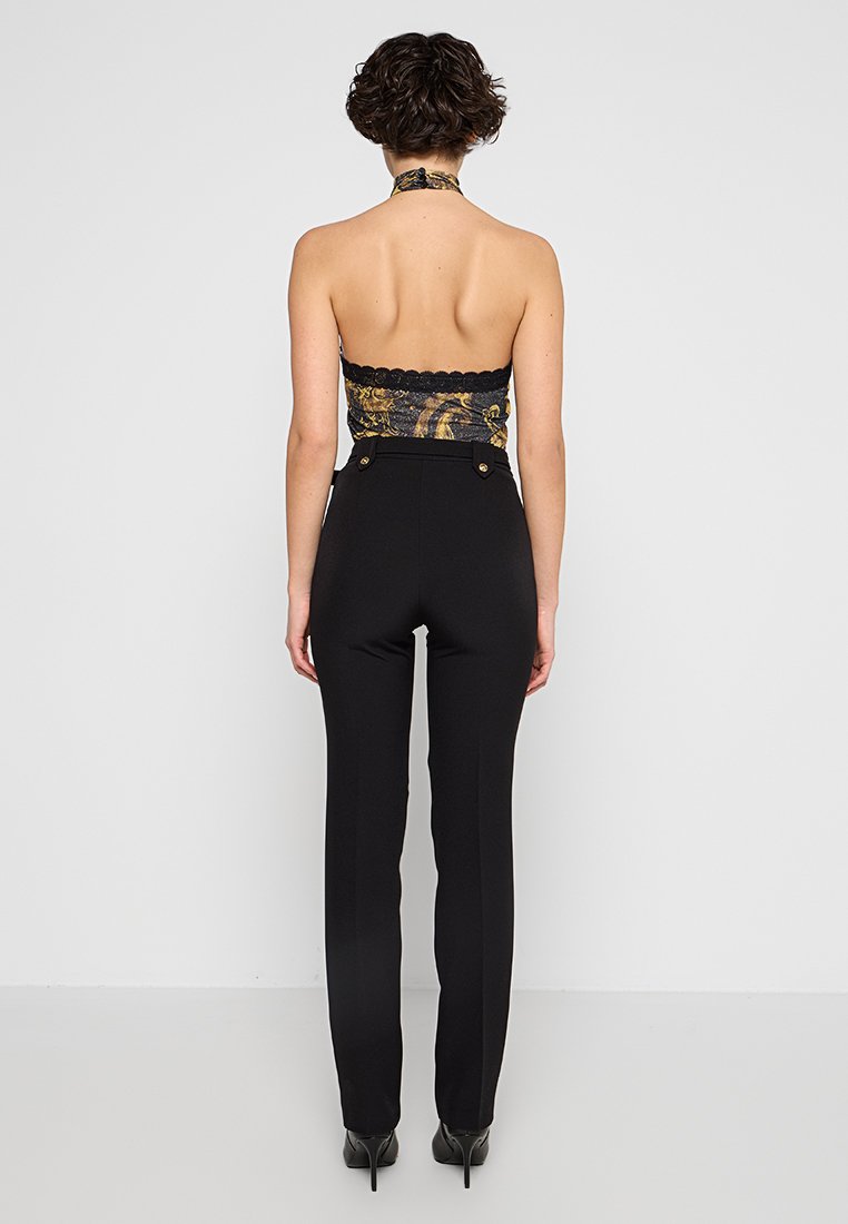 Pantalons noirs taille haute avec des accents de boutons dorés et un haut halter ajusté en crochet présentant des motifs dorés et noirs. Texture lisse.