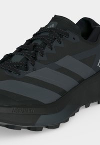 Μαύρο και σκούρο γκρι παπούτσι Adidas για τρέξιμο σε μονοπάτια με υφή στη σόλα, με λογότυπα ρίγες, κλείσιμο με κορδόνια και μεσαία σόλα με απορρόφηση κραδασμών "Lightstrike".