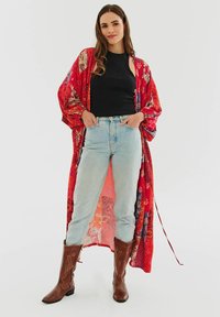 Červený vzorovaný kimono s širokými rukávy přes černý top, spárované se světle modrými džíny a hnědými kovbojskými botami. Kimono má květinové detaily.