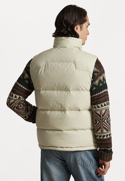 Colete beje volumoso com gola alta e mangas escuras em castanho padrão, apresentando designs geométricos em verde, castanho e creme.