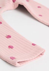 Bavoir en tissu côtelé rose avec des bords arrondis et de petits pois magenta dispersés sur la surface.