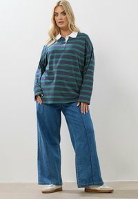 Mörkblå pikétröja med lång ärm, gröna och vita ränder, vit krage, kombinerad med vida blå jeans och ljusa sneakers.