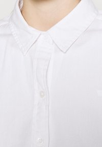 Vit skjorta med klassisk krage, med en enhetlig textur och tydliga, runda knappar längs den framre placket.
