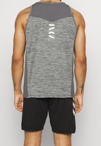 Canottiera atletica grigia con una texture melangiata e accenti grigi più scuri. Presenta un logo bianco e pantaloni corti neri a contrasto.
