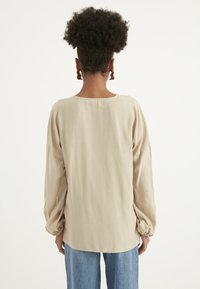 Helle beige Bluse mit langen Ärmeln, rundem Ausschnitt und elastischen Bündchen, kombiniert mit lockeren blauen Denim-Hosen. Glattes, leichtes Material.