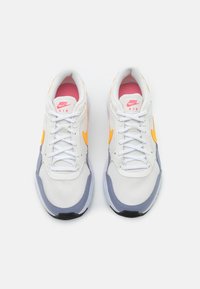 Vitaidrottssneakers i vitt med grå och orange detaljer, meshuppdelning, vadderad tunga och snörning, med en rosa inredning och svart sula.