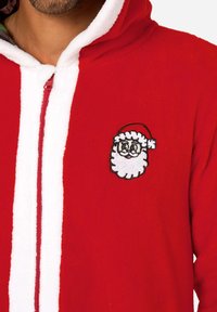 Rode fleece onesie met witte rits en kraag. Heeft een op de borst geborduurd zwart lui gezicht van de Kerstman. Zachte textuur, speels ontwerp.