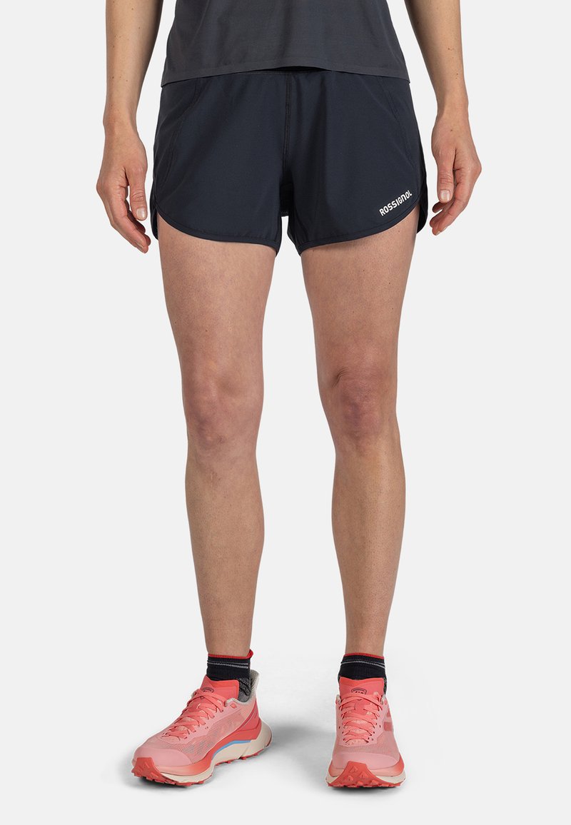 Pantaloni sportivi neri con orlo curvato, realizzati in tessuto leggero; abbinati a scarpe da corsa rosa con suola in gomma e tomaia in rete.