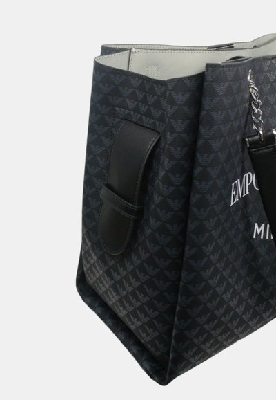 Große schwarze Tragetasche mit gemusterter Außenseite, Lederakzenten und einer silbernen Kette. Gestempeltes Logo auf der Vorderseite in Weiß.