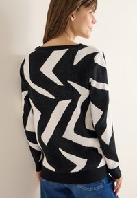 Musta-valkoinen siksak-kuvioitu neulepusero, jossa on pyöreä pääntie, pitkät hihat ja resorireuna. Neulottu rakenne, joka antaa rennon ilmeen.