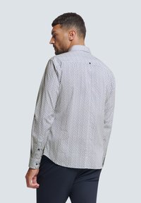 Herrenlangarmhemd in Weiß mit einem geometrischen Muster in Marineblau und Rot. Hat einen Kentkragen und Knopfmanschetten. Der Rücken hat ein kleines Schlaufen-Detail.