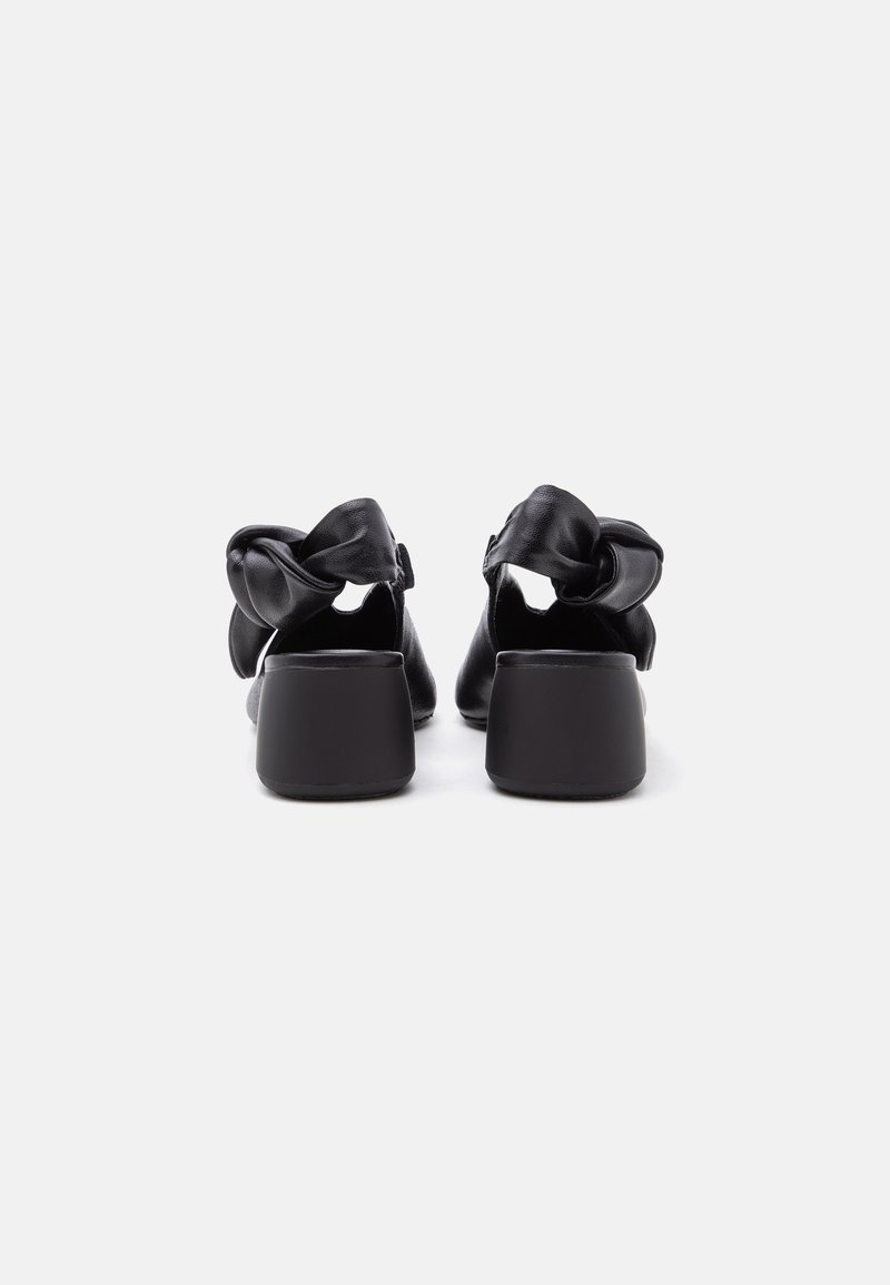 Paar schwarze Leder-Blockabsatzschuhe, von hinten mit gerafftem Schleifendetail an den Knöchelriemen gesehen.