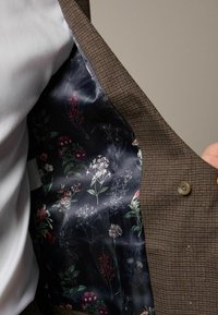 Braun karierter Blazer mit floral gemustertem dunklen Futter. Das Innenfutter hat eine satinartige Textur und eine auffällige Knopfverschluss.