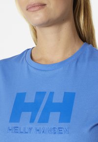 Camiseta de algodón azul con un gran logo tonal 'HH' y el texto 'HELly HANSEN' en bordado de contraste. Diseño de cuello redondo.