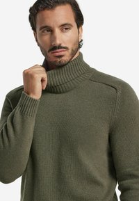 Zielono-oliwkowy sweter z golfem wykonany z miękkiej dzianiny, z prążkowanym kołnierzem i mankietami oraz luźnym fasonem z minimalnymi detalami szwów.
