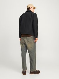 Μαύρο μπουφάν από μείγμα μαλλιού, ανοιχτό καφέ μπλούζα, ξεθωριασμένο μπλε τζιν, καφέ δερμάτινες μπότες και μπεζ καπέλο, απεικονίζεται από πίσω.