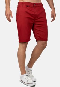 Rode katoenen shorts met omgerolde zomen, voorzien van een knoopsluiting aan de voorkant en zijzakken, gecombineerd met witte lage sneakers.