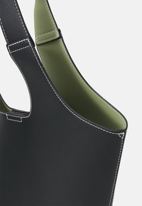 Černá kožená taška přes rameno s bílým prošíváním a olivově zeleným vnitřkem, zobrazující horní roh a ucha na bílém pozadí.