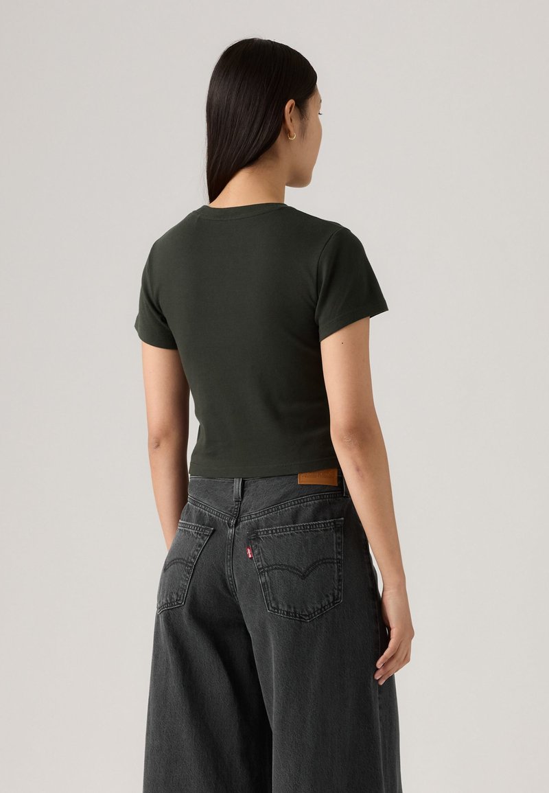 T-shirt court vert foncé à manches courtes, avec un col rond. Associé à un jean noir délavé à jambes larges, présentant des poches arrière.