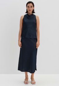Marineblauw mouwloos topje met een gedrapeerde neklijn, gecombineerd met een lange rok, beide gemaakt van gestructureerde stof met een zijsplit. Zilveren bandjesandalen.