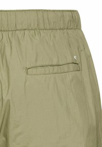 Licht olijfgroene shorts met een elastische tailleband, een enkele achterzak en een gladde, gestructureerde stof. Subtiele stikselaccenten zichtbaar.
