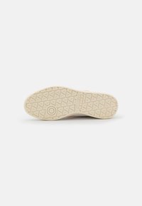 Podešev boty z béžové gumy s texturovaným povrchem, zdobená geometrickým vzorem a kruhovým logem uprostřed.