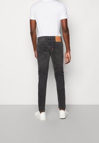 Musta farkkutakki slim fit -leikkauksella, jossa on nahkainen takapatch, kaksi takataskua ja hienovaraisia ompelutietoja. Yhdistetty valkoisen t-paidan ja valkoisten lenkkareiden kanssa.