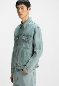 Light blue denim jacket with a collar, two chest pockets, and button closures. Textured finish; styled with matching denim bottoms.