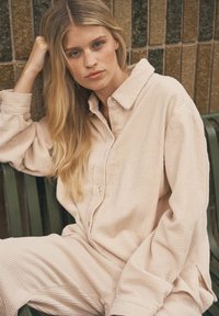 Beige Corduroy-Loungewear-Set mit einem knopfbaren Oberteil mit Kragen und locker sitzenden Hosen. Auffällige Rippstruktur und entspannter Schnitt.