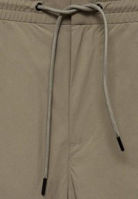 Shorts beiges avec une taille à cordon de serrage, présentant une texture lisse et deux poches latérales. Le cordon de serrage a des embouts en plastique.