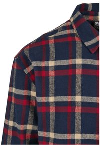 Chemise en flanelle bleu marine avec un motif à carreaux rouge et crème et un col replié, vue depuis l'épaule et la partie supérieure de la poitrine.