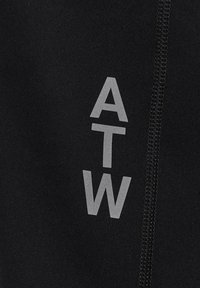 Schwarzer Stoff mit vertikalen reflektierenden Buchstaben "ATW" neben einer genähten Naht, die vertikal auf der rechten Seite verläuft.