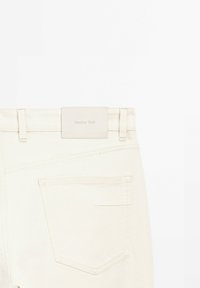 Jeans in denim beige con una superficie liscia e testurizzata. Presentano un'etichetta in pelle impresso con "Massimo Dutti" alla vita.