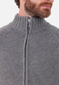 Pull gris en maille avec un col montant côtelé, une fermeture éclair frontale et un tissu texturé. Présente une finition lisse avec un motif côtelé vertical.