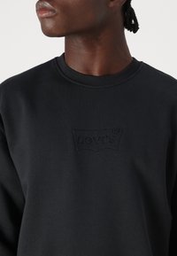 Μαύρο φούτερ κατασκευασμένο από μαλακό ύφασμα, με στρογγυλή λαιμόκοψη και ανάγλυφο λογότυπο Levi's στο στήθος. Απαλή υφή, casual σχεδίαση.