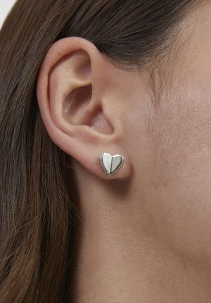 Herzförmiger Ohrstecker aus Silber mit glänzender weißer Einlage und schwarzem Akzent, umgeben von kleinen klaren Edelsteinen.