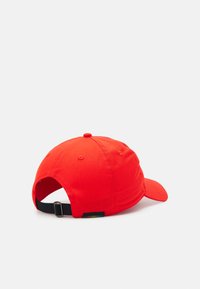 Red cotton baseball cap with a curved brim, adjustable black strap at the back, and a small tag featuring colored stripes on the side.
