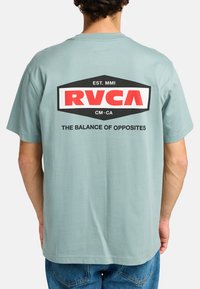 Turquoise cotton t-shirt featuring a large black and red RVCA logo on the back, with text reading "THE BALANCE OF OPPOSITES." Short sleeves.