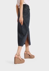 Gonna di jeans blu scuro con uno spacco laterale, abbinata a sandali con zeppa beige dotati di cinturini alla caviglia e una finitura liscia.
