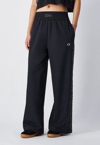 Zwarte wijde broek met een elastische tailleband en een logo. De zijstrepen hebben een golvend patroon. Gemaakt van een soepele, lichte stof.