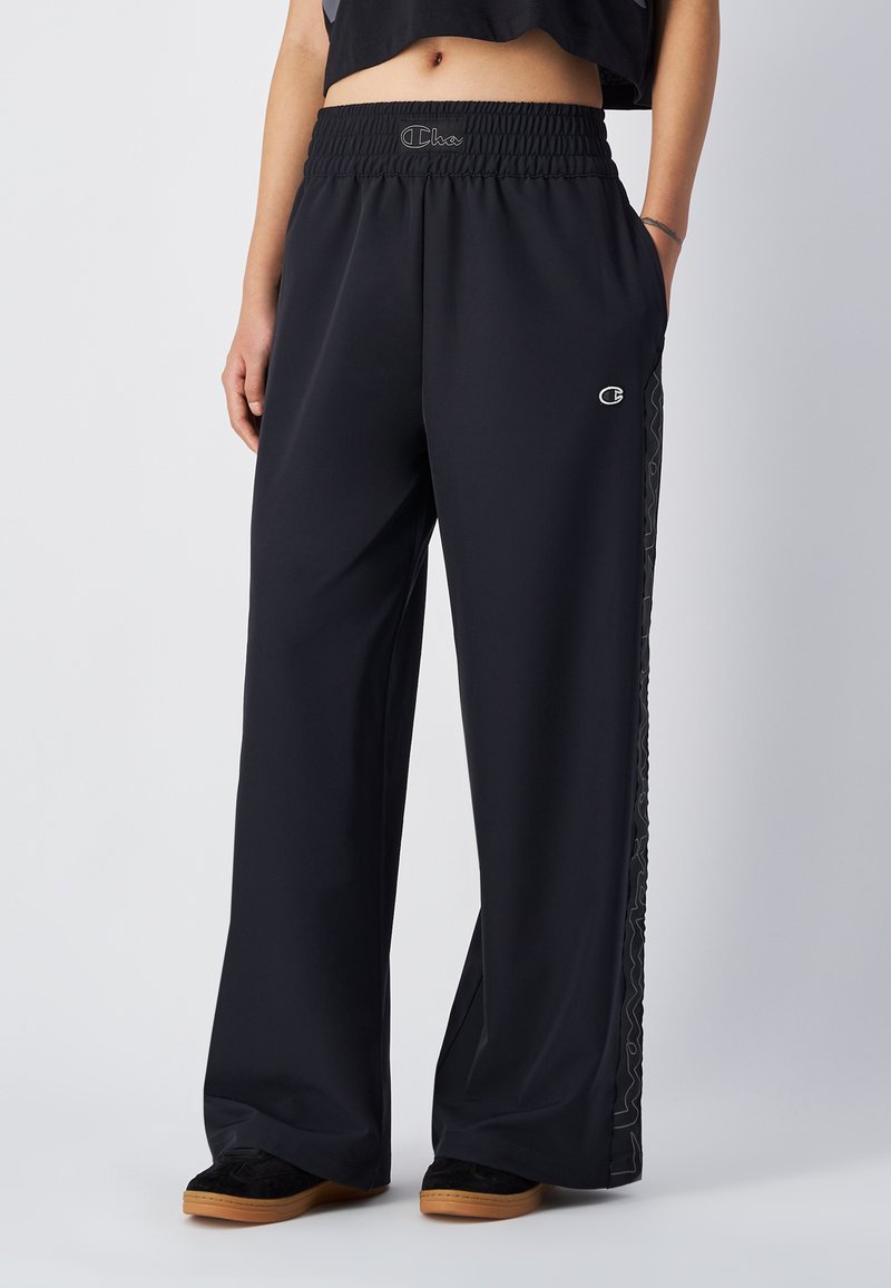 Zwarte wijde broek met een elastische tailleband en een logo. De zijstrepen hebben een golvend patroon. Gemaakt van een soepele, lichte stof.