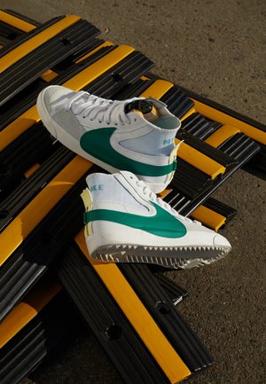 Weiße und türkisfarbene High-Top-Sneaker auf schwarzen und gelben Schwellen auf Asphaltboden platziert.