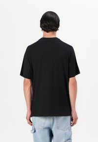 T-shirt noir à manches courtes avec une coupe droite, présentant un col rond et un tissu doux. Détails de couture visibles aux coutures des épaules.