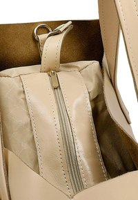 Beige leren handtas interieur met een ritscompartiment, met een glanzende rits en een gestikte patroon op de voering. Zachte suède textuur.