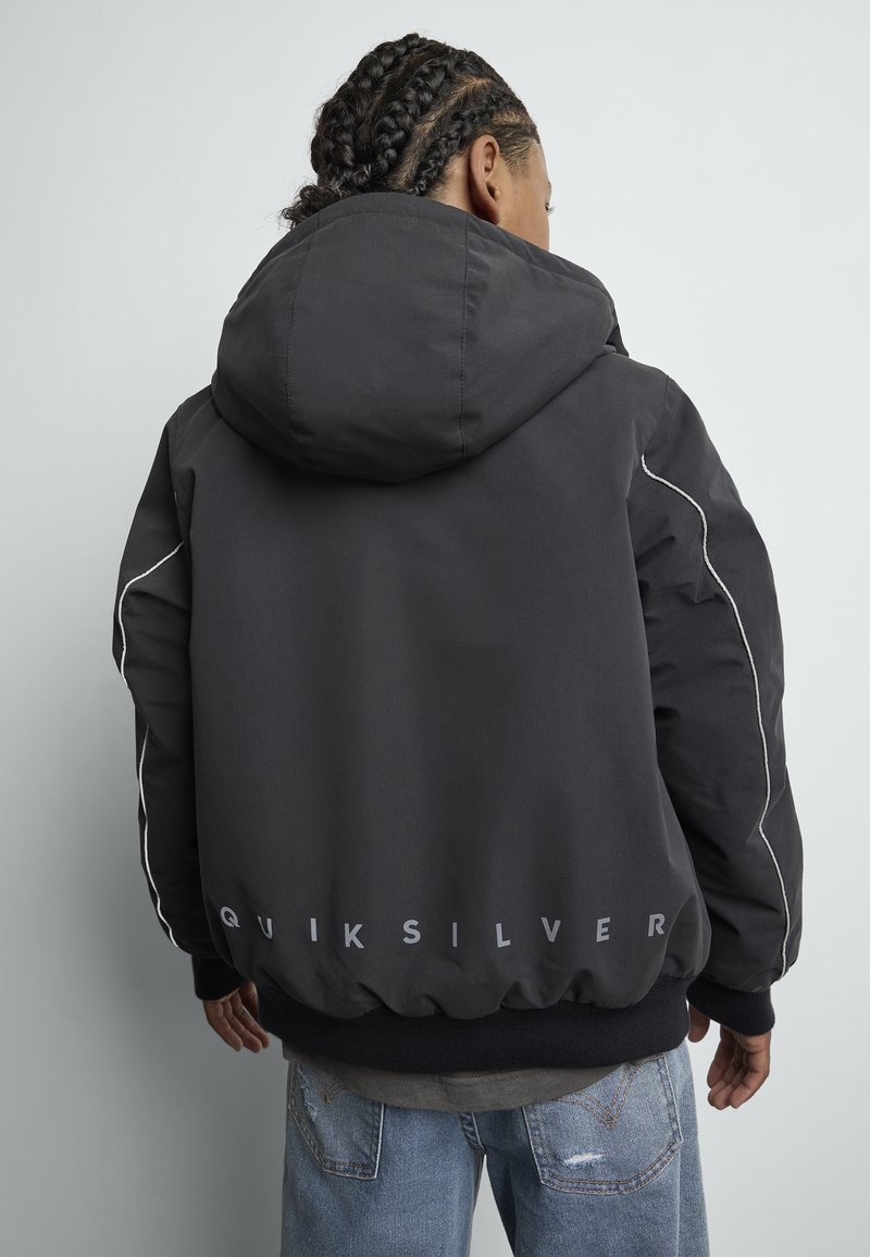 Μαύρο μπουφάν με κουκούλα και λευκές λεπτομέρειες, ελαστική μέση και λογότυπο "QUIKSILVER" στο πίσω μέρος. Το υλικό φαίνεται λείο και ανθεκτικό.