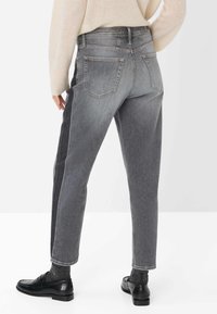 Graue Jeans mit hoher Taille, die leicht locker geschnitten sind und seitliche Akzente in einer dunkleren Farbnuance aufweisen. Robustes Denim-Material und klassisches Fünf-Taschen-Design.